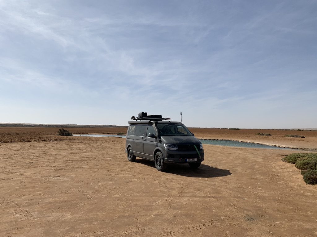 Expedition vehicle parked beside a desert waterhole